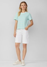 Gestreept T-shirt met korte mouwen in lichtblauw en wit, gecombineerd met opgerolde witte bermuda shorts en beige sneakers. Casual, ontspannen pasvorm.
