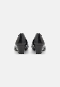 Chaussures à talons noirs en cuir lisse, avec un bout rond et un talon carré de hauteur moyenne. L'arrière présente un détail de couture subtil.