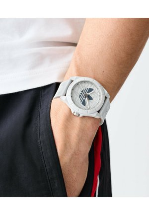 Balta silikoninė apyrankė su raštuotu ciferblatu, dideliais valandų žymenimis ir mėlynais akcentais. Apyrankė yra tekstūruota, o dizainas sportiškas.
