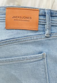 Jeans in denim azzurro chiaro con un'etichetta in pelle color cuoio, impressa con "JACK & JONES JEANS INTELLIGENCE", caratterizzati da un classico design a cinque tasche.