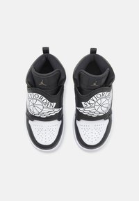 Black and white athletic shoes featuring a high-top design, perforated toe box, and a prominent strap with a winged logo.