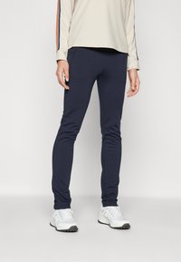 Marina träningsbyxor med en figurnära design, två framfickor och ett elastiskt tyg. Kombineras med en beige långärmad topp och vita sneakers.