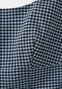 Tissu à carreaux noir et blanc avec une couture et un pli, montrant la texture et le motif sur une section de vêtement.