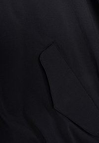 Sort tekstureret stof med et vinklet lomme-design, der er sømløst integreret i beklædningen, med et subtilt, uregelmæssigt mønster.