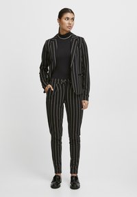 Svartvit randig skräddarsydd kostym med en kavaj och figursydda byxor, tillverkad av ett slätt tyg med en elegant finish.