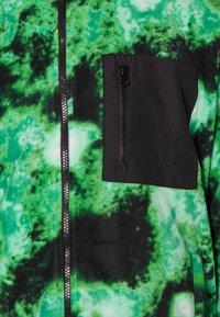 Giacca in pile verde e nera con motivo tie-dye. Presenta una tasca con zip nera e una cerniera frontale a tutta lunghezza. Texture morbida.