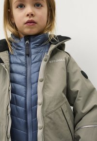 Lichtgrijze buitenjas met een blauwe geïsoleerde binnenlaag, voorzien van drukknoopjes, een rits aan de voorkant en een zwarte kraag.