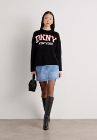Černý pletený svetr s červeným nápisem "DKNY NEW YORK", modrá džínsová mini sukně, černé kozačky po kolena a malá černá kabelka.