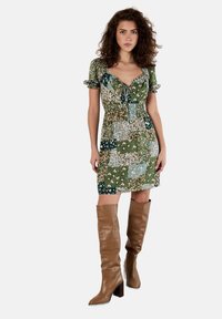 Blumendruckkleid in grünen und blauen Tönen, mit kurzen Puffärmeln, einer Knopfleiste vorne und einem elastischen Taillenbund, kombiniert mit braunen kniehohen Stiefeln.