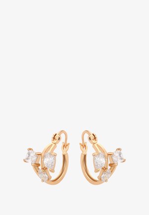 Gli orecchini a cerchio color oro presentano due pietre trasparenti a forma geometrica e una pietra a forma di pera, evidenziando un design elegante e moderno.
