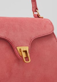 Sac à main en daim rose avec un rabat arrondi, quincaillerie dorée et un fermoir distinctif. Texture lisse et détails cousus le long des bords.