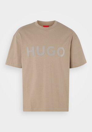Beżowa bawełniana koszulka z okrągłym dekoltem i krótkimi rękawami. Na przodzie wyraźnie widnieje napis "HUGO" w szarym kolorze. Gładka faktura.