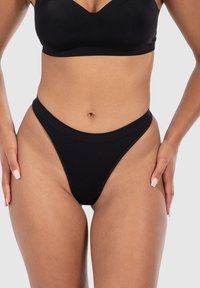 Schwarze Tanga-Unterwäsche mit einem hochgeschnittenen Design, nahtlosen Kanten und weichem Stoff, der die Taille und Hüften betont.