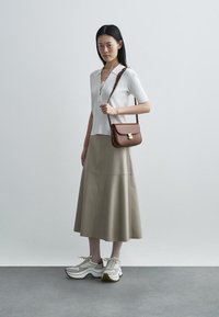 Valge soonikkoega lühikeste varrukatega särk, beežis laienev seelik, pruun kuldse riistvaraga rihmkott ja kreemikad tossud tekstureeritud valge viimistlusega.