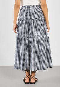 Zwart-witte ruitjes maxi rok met meerdere lagen en een aansluitende taille, met ruches aan de naden en een vloeiende silhouet. Platte sandalen zichtbaar.