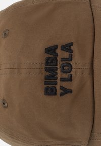Gorra de algodón marrón con texto bordado en negro "BIMBA Y LOLA". Visera plana, diseño estructurado y ojales de ventilación en la parte superior.