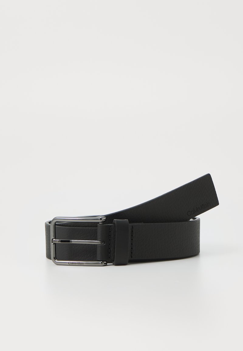 Zwarte leren riem met een gestructureerde afwerking, voorzien van een zilveren metalen gesp. Het einde loopt taps toe naar een vlakke punt. Het merkembleem is vlakbij de gesp gegoten.
