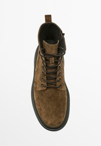 Bottine en daim marron avec un design à lacets noirs, bout rond et semelle en caoutchouc contrastante. Dotée d'une languette pour faciliter l'enfilage.