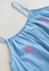 Haut sans manches en denim bleu clair avec fines bretelles et motifs brodés de palmiers roses sur le devant.