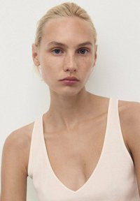 Hellrosa Tanktop mit tiefem V-Ausschnitt und dünnen Trägern, aus einem weichen Stoff gefertigt. Das Design zeichnet sich durch klare Linien und eine glatte Textur aus.