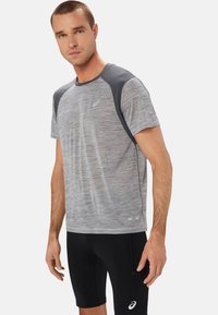 T-shirt atletico a maniche corte grigio melange con pannelli sulle spalle grigio scuro, abbinato a pantaloni corti compressivi neri con un logo sulla gamba.
