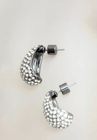 Cercei inelari negri din metal, ornamentați cu cristale claire, având o formă curbată și accesorii de culoare argintie. Suprafața texturată adaugă detalii.
