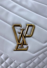 Cuoio bianco trapuntato con linee diagonali, con un accentuato logo dorato al centro. Dettaglio testurizzato sullo sfondo.