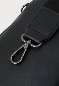 Black leather bag detail featuring a metallic clip and textured strap with stitching accents for added durability.