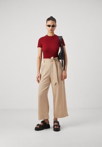 Rode korte mouwen top, beige wijde broek met strikriem, zwarte tas met studs en chunky zwarte sandalen met gespen.
