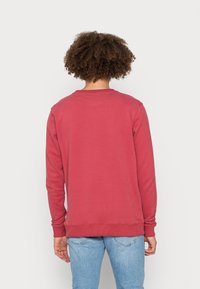 Red cotton sweatshirt with long sleeves and a round neck. Features ribbed cuffs and bottom hem, smooth texture, and simple design.