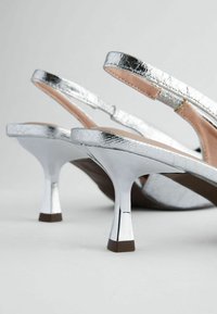 Hopeat slingback-kengät, joissa on kiiltävä metallipinta, teräväkärkinen muotoilu ja hoikka korkea korko, jossa on teksturoitu pinta.