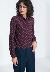 Burgundowa koszula z guzikami, w różowe kropki, z długimi rękawami, kołnierzykiem i pojedynczą kieszenią na piersi, zestawiona z granatowymi spodniami o wysokim stanie.