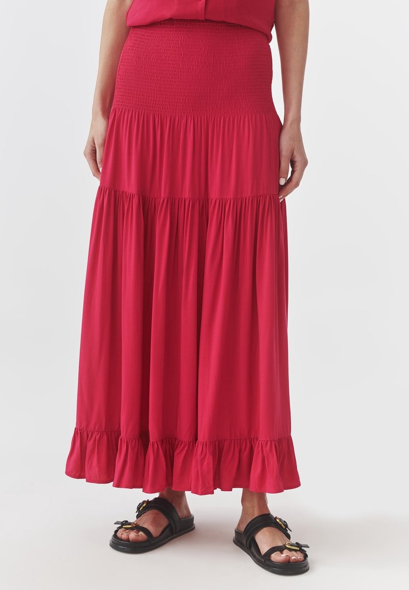 Rode maxi rok van een zachte, rekbare stof. Kenmerkt een smocktaille, gelaagd ontwerp en een gerimpelde zoom. Gedomineerd met zwarte sandalen.