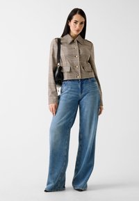 Veste courte en plaid beige avec des boutons dorés et deux poches avant, associée à un jean denim bleu ample en denim clair.