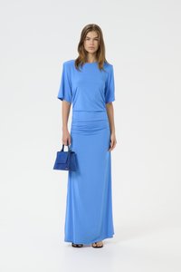 Blue maxi dress with short sleeves and gathered waist; smooth fabric; paired with a small blue handbag; sandals on feet.