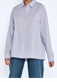 Camicia button-up di un leggero lilla con maniche lunghe, colletto classico e taglio dritto. Presenta una texture liscia e piccoli bottoni trasparenti.