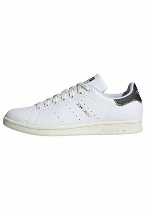 Białe buty sportowe Adidas Stan Smith z czarną wstawką na pięcie, złotymi literami, białymi sznurowadłami i perforowanymi bocznymi paskami.