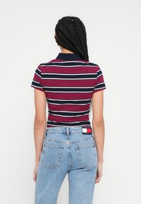 Pruhované polokošeľa v burgundskej, námorníckej modrej a bielej farbe s golierom. Nosí sa s svetlomodrými džínsami z denimu, ktoré majú klasický strih a textúru.