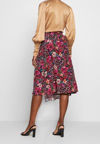 Jupe fleurie avec un ourlet asymétrique en teintes vives de rose, violet et orange sur un fond sombre ; associée à un blouse en satin beige.
