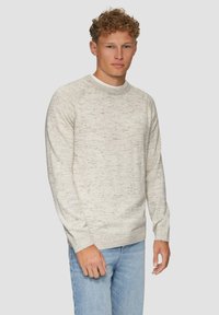 Lichtgrijze, gespikkelde crewneck trui met lange mouwen en geribbelde manchetten. Gecombineerd met lichtblauwe jeans. Soepele textuur.