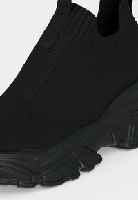 Baskets noires à enfiler avec dessus en maille texturée et semelle épaisse avec des rainures profondes pour une bonne adhérence.