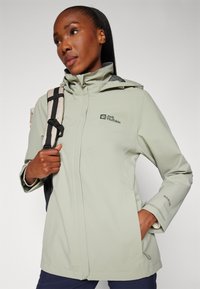Light green jacket made of Texapore material, features a hood, zip closure, and elastic cuffs. Logo on chest and shoulder.