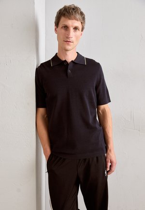 Dark polo shirt with short sleeves and a contrasting collar. Smooth texture, two-button placket. Paired with black pants featuring side accents.