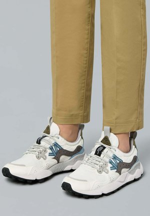 Weiße Sneakers mit grauen und blauen Akzenten, strukturierten Überzügen und einer klobigen schwarzen Sohle. Die Schnürsenkel und der gepolsterte Kragen runden das Design ab.