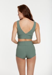 Reggiseno sportivo verde a coste con schiena a V profonda, abbinato a pantaloni corti a vita alta. Entrambi presentano una texture liscia e pochi dettagli metallici.