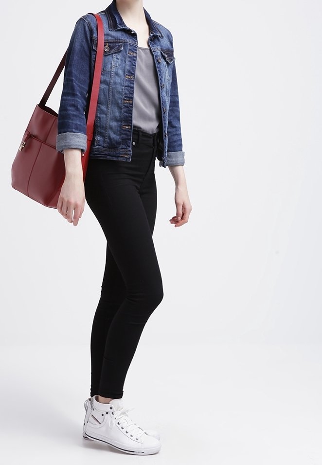 Osoba ubrana w kurtkę jeansową, szarą koszulę, czarne spodnie i białe wysokie trampki, niosąca dużą czerwoną torbę na ramię.