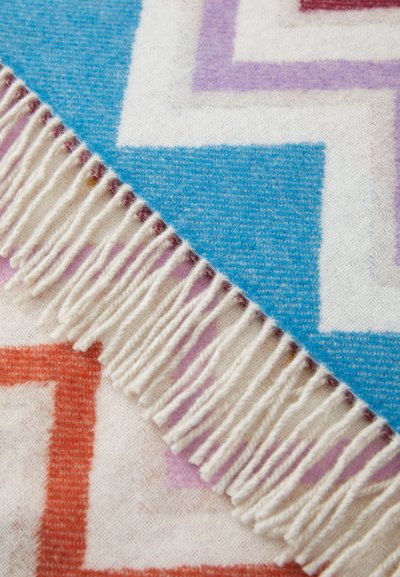 Woven wool blanket with geometric patterns in blue, orange, and purple, featuring white fringes along one edge. Soft texture.