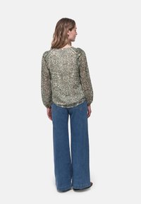 Blusa verde a maniche lunghe, stampata, realizzata in tessuto trasparente, abbinata a jeans in denim blu a gamba larga. La blusa presenta un collo rotondo e maniche arricciate.