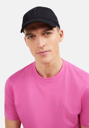 Casquette de baseball noire à visière incurvée, design structuré et détail logo discret. Associée à un t-shirt à col rond rose uni.