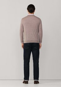 Lichtbruine gebreide trui met een ronde halslijn, geribde manchetten en zoom, gecombineerd met donkerdenim jeans en bruine schoenen.